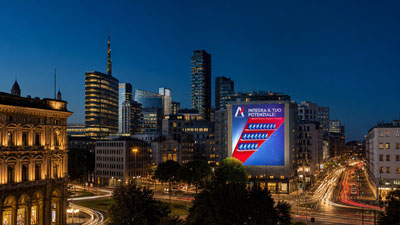 Night cityscape with modern high-rises and a large illuminated billboard on a tall building, with blurred car lights along the street.