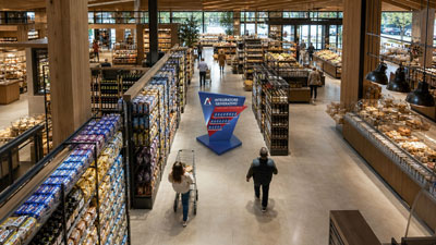 A spacious modern bookstore with tall shelves, customers browsing, and a blue geometric display in the center.