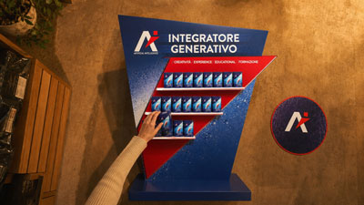 Blue angled display labeled Integratore Generativo with red shelves holding rows of small blue cards; a person’s arm reaches toward it; round logo on the floor nearby.