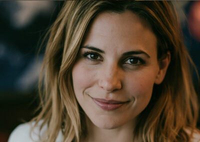 Close-up portrait of a woman smiling softly, with light brown hair and a warm, blurred background.