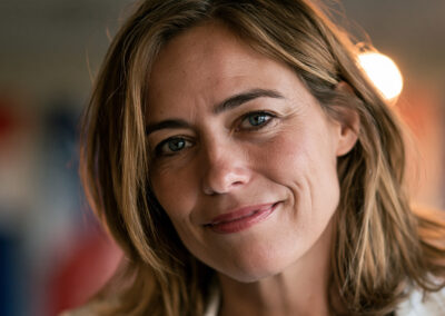 Close-up portrait of a smiling woman with light brown hair and blue eyes, soft blurred background.